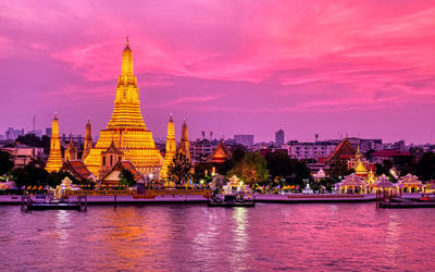 Illuminated temple building by river against sky