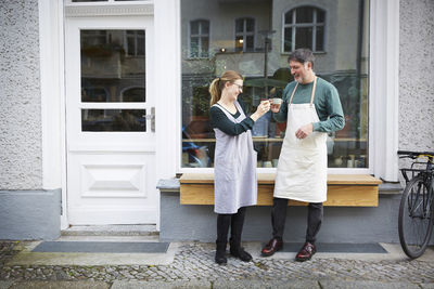 Smiling male and female colleagues toasting coffee outside art studio