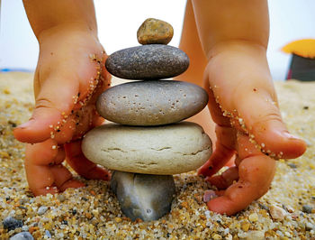 Copped hands of child stacking pebbles at beach