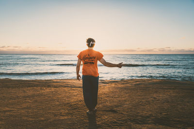 Rear view of man standing on beach during sunset