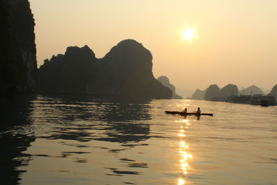 People canoeing on halong bay by rock formations against clear sky