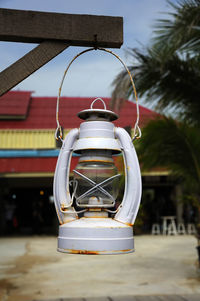 A gray oil lamp hanging under a wooden beam, on a blureed background.