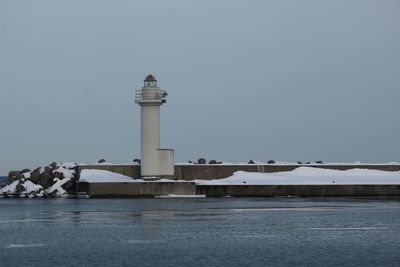 Lighthouse by sea against clear sky