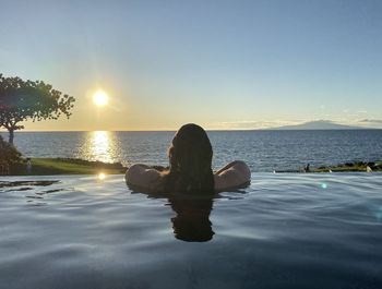 Woman relaxing in infinity pool against sea during sunset