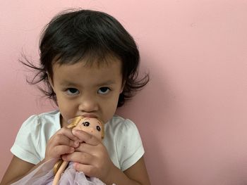 Portrait of cute girl biting toy against wall