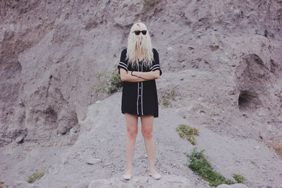 Full length of woman with arms crossed and covered face standing against rock