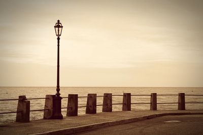 Street light on wooden post by sea against sky