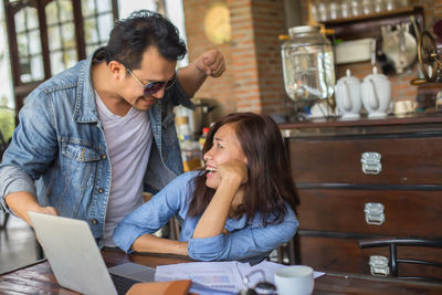 Cheerful business people using laptop while sitting in cafe