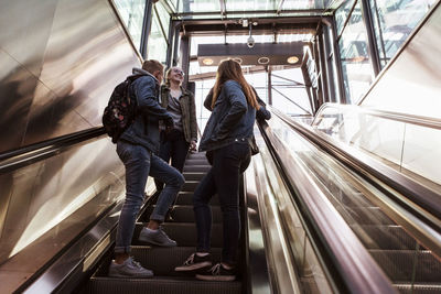 Low angle view of teenage friends talking while standing on escalator