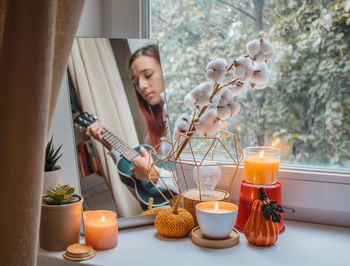 Girl sits in her room on window sill and plays ukulele. home decoration for thanksgiving, halloween