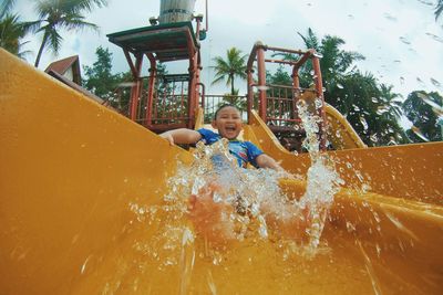Low angle view of boy playing on water slide at park