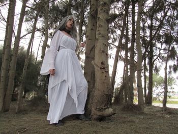 Woman standing by tree trunk in forest