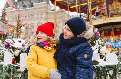 Brother and sister looking away while standing by christmas tree