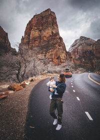 People on road by rock formation against sky