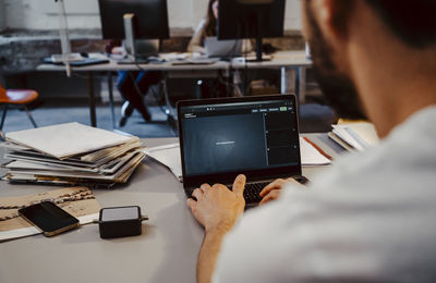 Male programmer coding on laptop at desk in startup company