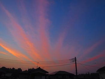 Low angle view of silhouette electricity pylons against orange sky