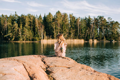 Man sitting on rock by lake against trees