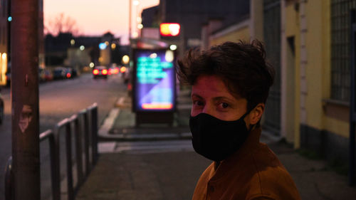 Portrait of woman with short hair standing on street at night wearing a mask