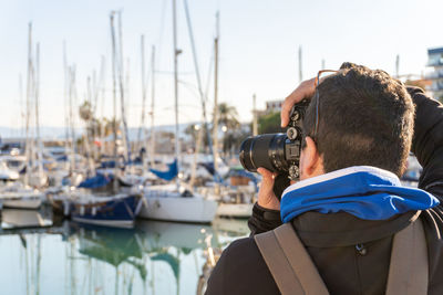 Rear view of a man taking photos in an indiscreet way with a professional camera with a zoom lens.