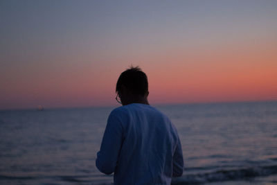 Rear view of man looking at sea during sunset