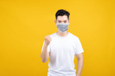 Portrait of young man standing against yellow background