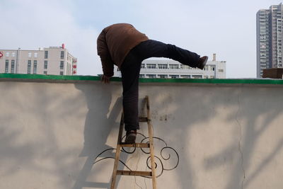 Low angle view of man climbing on wall with help of ladder
