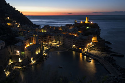 High angle view of illuminated townscape by sea against sky during sunset