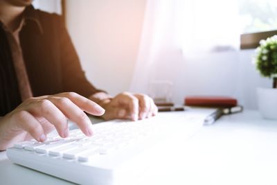 Cropped image of businesswoman typing on keyboard at table in office