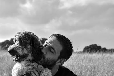 Portrait of man with dog on field against sky