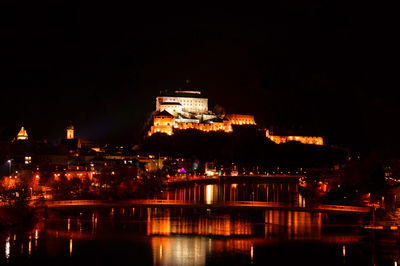 Illuminated city by river against sky at night