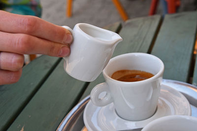 Cropped hand pouring milk from pitcher in coffee at table