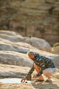 Blonde man scoops water from a shallow puddle in the desert