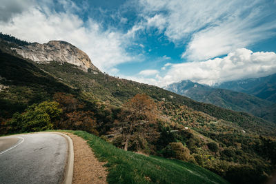 Country road by mountains against sky