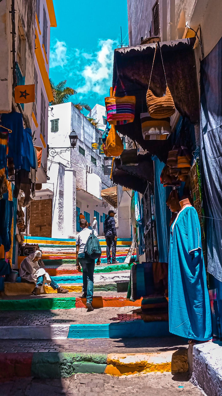 REAR VIEW OF PEOPLE WALKING ON STREET AGAINST BUILDINGS