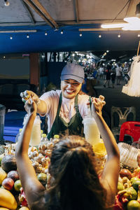 Smiling female vendor giving juice glasses to girl at food market