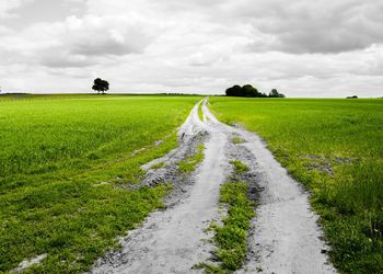 Road passing through field against cloudy sky