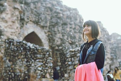 Young woman looking up while standing against old ruin