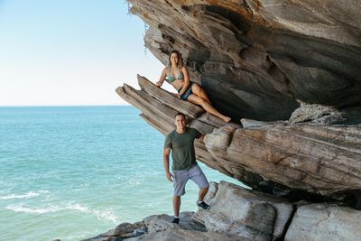Woman standing on rock by sea against sky
