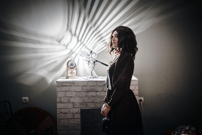Side view of woman standing against wall at home