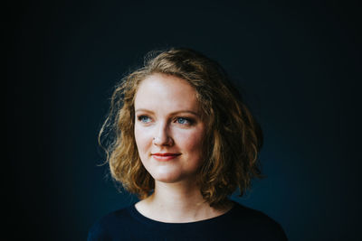 Close-up of thoughtful woman smiling while looking away against wall