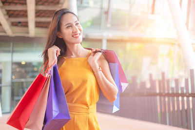 Smiling young woman holding umbrella while standing on store