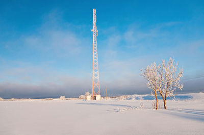 Communications tower on snow covered land against sky