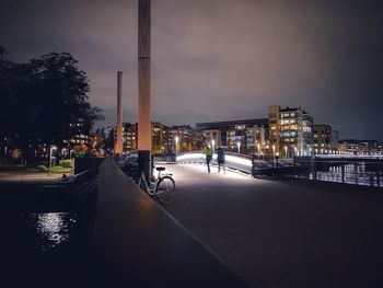 Illuminated street by buildings against sky at night