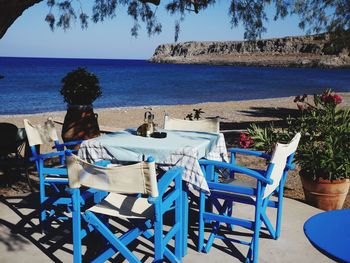 Chairs and tables at beach against blue sky