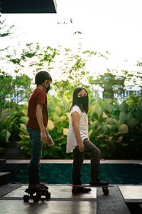 Two asian children wearing mask skateboarding in the outdoor.