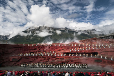 Group of people in front of buildings against cloudy sky