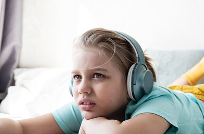 Cute boy listening to music in earphones lying on bed. child wearing headphones listens to music.