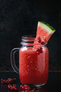 Close-up of juice with watermelon and red currants on table against wall