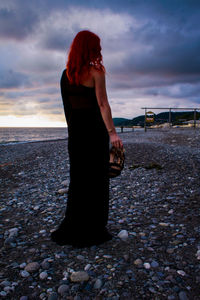 Woman standing at beach against sky during sunset