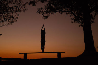 Silhouette man with arms raised against sky during sunset